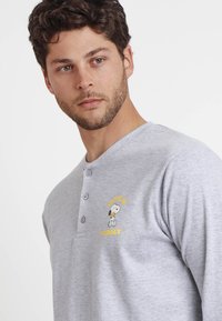 Camisa henley de manga larga gris, hecha de algodón suave, con una impresión amarilla de Snoopy y el texto "Bonito y Adorable" cerca del pecho. Con tapeta de tres botones.