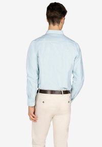 Camisa de rayas azul claro con mangas largas, puños abotonados y cuello de punta, combinada con pantalones color crema y un cinturón marrón oscuro.