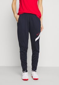 Marina atletiska joggers med röd Nike-logotyp och vit randdesign, med elastisk midja och sidofickor. Slät polyesterstoff.