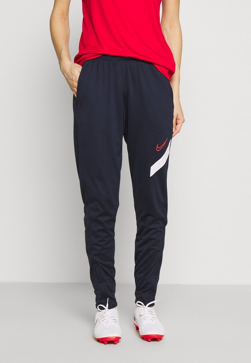 Marina atletiska joggers med röd Nike-logotyp och vit randdesign, med elastisk midja och sidofickor. Slät polyesterstoff.