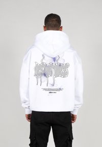 Hvid hoodie med et stort grafisk design på ryggen, der viser lilla sommerfugle og stiliseret tekst. Blødt stof, snor til hætten og afslappet pasform.
