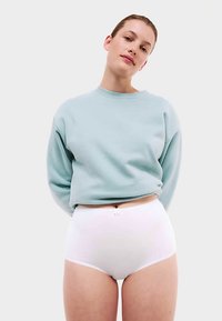 Felpa corta azzurro chiaro con maniche lunghe, abbinata a slip bianchi a vita alta con un delicato fiocco decorativo sulla fascia in vita.