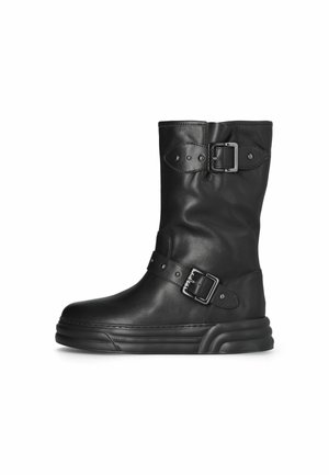 Stivale alla caviglia in pelle nera con punta arrotondata, due fibbie decorative e suola spessa. Presenta una texture liscia e un design minimalista.