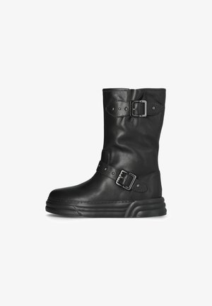 Stivale alla caviglia in pelle nera con punta arrotondata, due fibbie decorative e suola spessa. Presenta una texture liscia e un design minimalista.