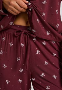 Bordeaux pyjama set gemaakt van zachte stof, met witte strikontwerpen en stippen. Bevat een losse top en broek met elastische taille.