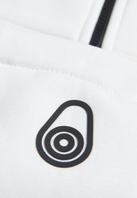 Tela blanca con un acabado texturizado que presenta un acento de logo de caucho negro en una forma abstracta con círculos concéntricos.