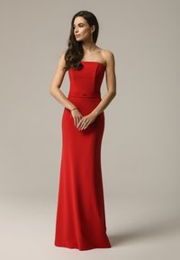 Czerwona wieczorowa sukienka bez ramiączek z dopasowanym gorsetem, zwiewną spódnicą i subtelnym pasem w talii. Gładki materiał z elegancką sylwetką.