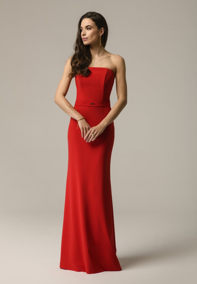 Czerwona wieczorowa sukienka bez ramiączek z dopasowanym gorsetem, zwiewną spódnicą i subtelnym pasem w talii. Gładki materiał z elegancką sylwetką.