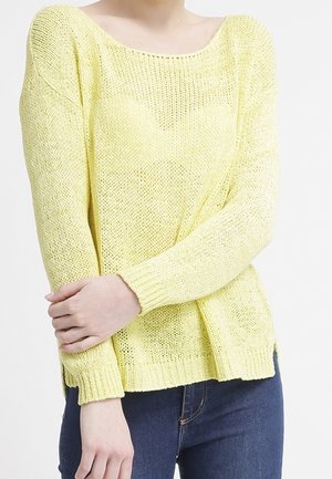Pull en maille jaune avec un décolleté large et des manches longues, offrant une coupe ample et un ourlet côtelé, associé à un jean foncé.