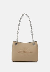 Beige handväska med en slät yta, som har ett silverfärgat kedjehandtag och ett präglat "CK"-logotyp, med "Calvin Klein Jeans" tryckt på framsidan.