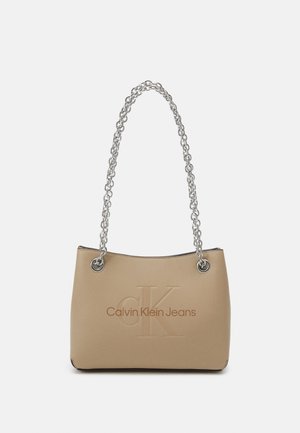 Beige kabelka s hladkou texturou, se stříbrným řetízkem a embosovaným logem "CK", s nápisem "Calvin Klein Jeans" na přední straně.