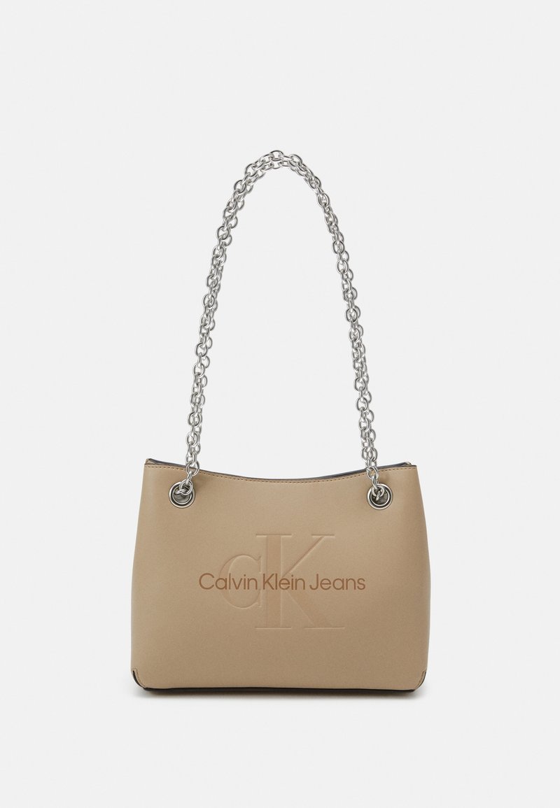 Beige handväska med en slät yta, som har ett silverfärgat kedjehandtag och ett präglat "CK"-logotyp, med "Calvin Klein Jeans" tryckt på framsidan.