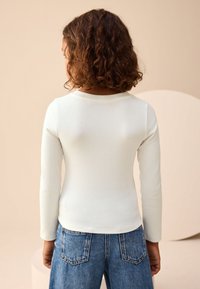 Haut à manches longues en maille côtelée de couleur crème clair, avec un col rond et une coupe ajustée, associé à un short en denim taille haute avec poches.