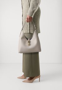 Borse hobo in pelle liscia grigia chiara con forma curvata, chiusura in metallo dorato e manico corto; indossata con pantaloni oliva e décolleté nude.