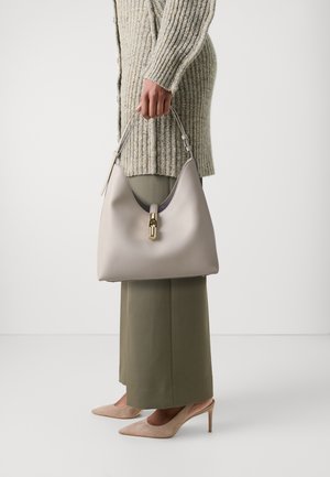 Sac hobo en cuir lisse gris clair avec une forme incurvée, fermoir en or, et une courte poignée ; porté avec un pantalon olive et des talons nus.