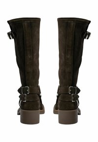 Botas de ante marrón oscuro hasta la rodilla con dos correas ajustables y hebillas plateadas. Tacón grueso. Textura suave con un diseño limpio.