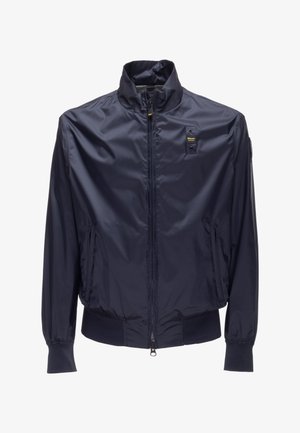 Giacca leggera blu navy con zip frontale, colletto alto, polsini elastici, due tasche frontali con zip e un piccolo logo rettangolare sul petto.