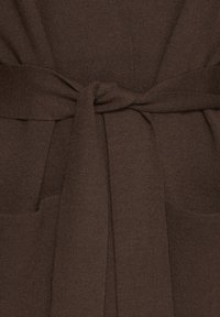 Primo piano di una cintura di tessuto lavorato a maglia marrone annodata attorno a un punto vita, con texture a maglia visibile.