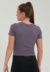 Lila ribbad t-shirt med kort ärm och rund halsringning, åtsittande silhuett och cropped längd, ihop med svarta högmidjade leggings.