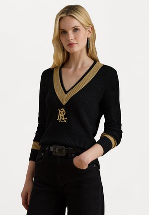 Svart stickad tröja med en guld V-ringning och manschetter, samt en guld logotypdetalj på framsidan. Bärs tillsammans med svarta byxor och ett bälte.