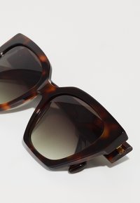 Sunglasses iz tortoiseshell s prenapihnjenimi geometrijskimi okvirji, temnih gradientnih lečah in sijajnim zaključkom. Vsebujejo zlat poudarek na tempeljih.