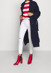 Abrigo de lana azul oscuro, camisa a rayas rojas y blancas, jeans blancos rotos y botas de tobillo de cuero rojo con paneles laterales negros y tacones de bloque.