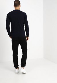 Marinblå crewneck-tröja med långa ärmar, kombinerad med svarta joggers. Plagget har en slim fit och vita sneakers. Slät textur på tyget.