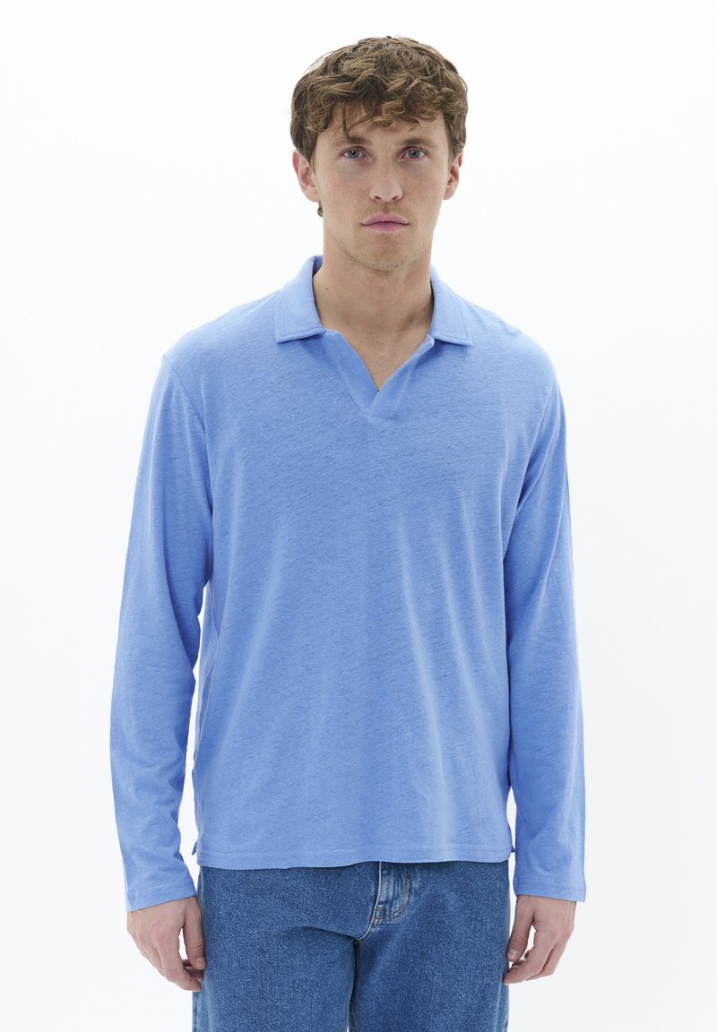 Light blue long-sleeve polo shirt with a V-neck and soft texture. Worn with blue jeans, featuring a relaxed fit and casual style.