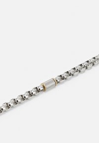 Bracelet en chaîne en argent avec un élément central en métal texturé et un accent doré. Le design est entrelacé avec des maillons lisses et polis.