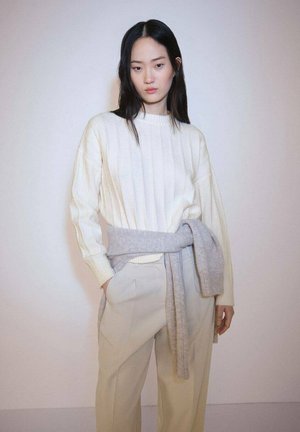 Cream ribbed sweater with a high neck, paired with light gray slacks. A soft gray tie-around sweater accentuates the waist. Smooth fabric texture.