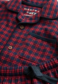 Rød og marineblå ternet flanell pyjamasæt med træknapper, krave, lappedetalje og snøre i taljen. Blød tekstur synlig.