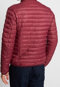 Bordeauxrote Steppjacke mit horizontalen Steppnähten, hohem Kragen und elastischen Bündchen. Glatter, glänzender Stoff mit eng anliegender Passform.