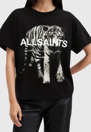 Vrouw draagt een zwart T-shirt met een grote witte tijgerafbeelding en gedurfde tekst "ALLSAINTS LONDON" op de voorkant.