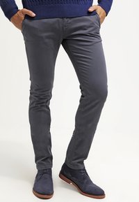 Grijze slim-fit broek van gladde stof, met een strak ontwerp en zijzakken, gecombineerd met marineblauwe suède schoenen en een blauwe trui.