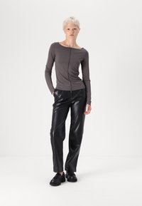 Haut gris à manches longues avec un décolleté carré et une couture centrale, associé à un pantalon en cuir noir avec des panneaux structurés et une coupe décontractée.