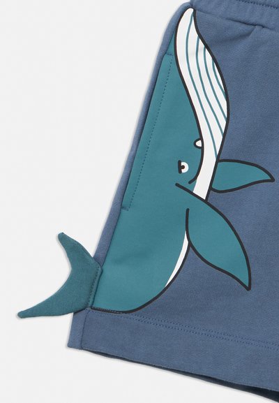 Tissu bleu avec une baleine bleue imprimée affichant un visage souriant et des nageoires, avec une nageoire caudale 3D attachée sur le côté.