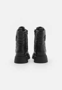 Zwarte enkelboots met een gladde leren afwerking, gewatteerde accenten op de achterkant, stevige rubberen zolen en ritssluitingen aan de zijkanten.