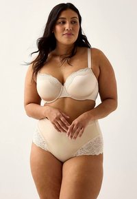 Set med beige behå och höga trosor prydda med spets. Mjuk tyg, följsam textur och blommig spetsdetalj längs kanterna. Elegant och kvinnlig design.