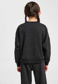 Svart sweatshirt av texturerat tyg med subtila glittrande detaljer, med lös passform, långa ärmar och ribbade muddar och nederkant.