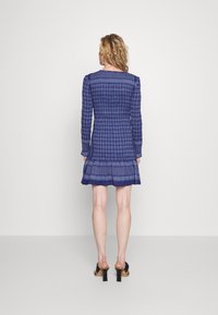 Námořnický modrý šaty s dlouhými rukávy, texturovaný vzor houndstooth, vrstvený volánkový lem a vyšívané akcenty podél výstřihu a manžet.