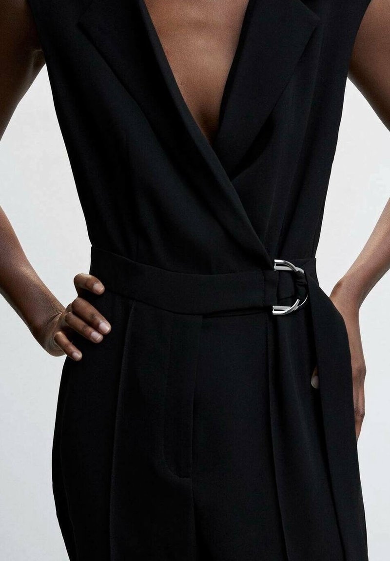 Zwarte jumpsuit met een diepe V-hals, wikkeldesign en een brede riem met zilveren gesp. Zachte, matte textuur met een getailleerde pasvorm.