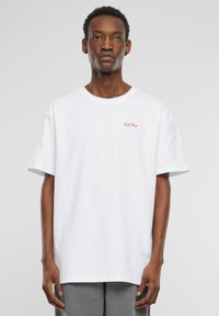 T-shirt en coton blanc à manches courtes, avec un texte rouge "Ball Fluid" sur la partie gauche de la poitrine. Design simple et décontracté.