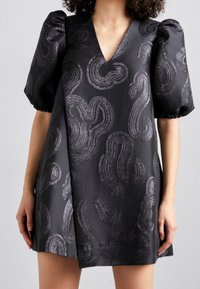 Schwarzes Kleid mit V-Ausschnitt, kurzen Puffärmeln und strukturierten wellenförmigen Mustern aus glänzendem Material, mit lockerem Schnitt und geradem Saum.