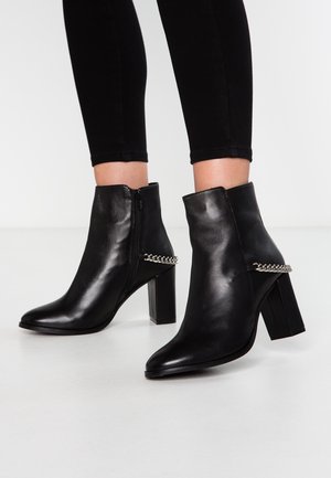 Schwarze Stiefeletten mit spitz zulaufender Spitze, Reißverschluss, strukturiertem Leder, Blockabsatz und silberner Kettenverzierung an der Seite.