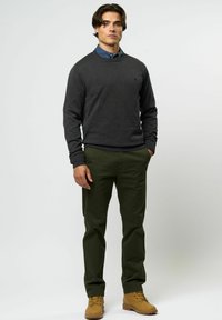 Tumši pelēks džemperis ar ribotām piedurknēm uz viegli zilās krekla ar apkakli, kombinēts ar olīvzaļām biksēm un brūnām zābakiem. Ikdienas pielaide un faktūras audums.