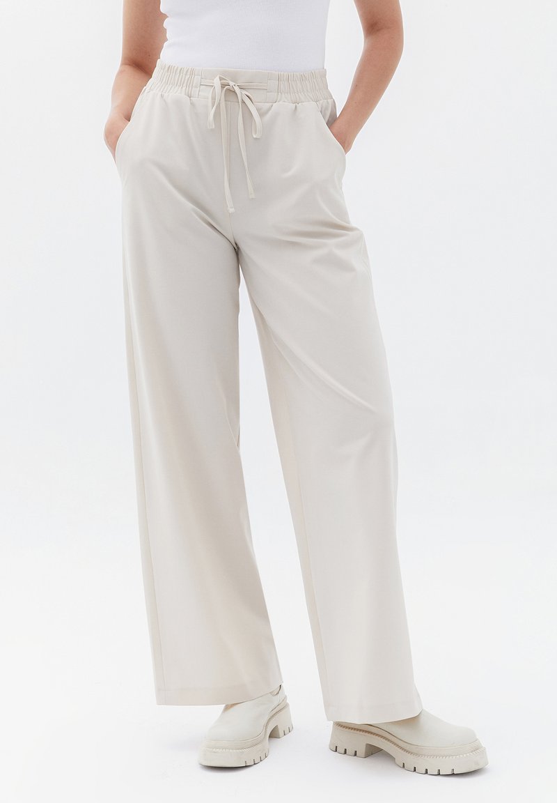 Krémové kalhoty s širokými nohavicemi, elastickým pasem a šňůrkou, s bočními kapsami a hladkým, lehkým textilním vláknem.