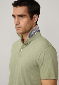 Ljusgrön polo skjorta med en texturerad yta, med ett blommönster på insidan av kragen och en tvåknapps knäppning.