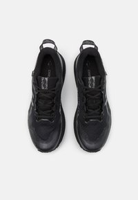 Scarpe sportive nere con tomaia testurizzata, lacci e dettagli riflettenti. Presentano una suola ammortizzata e una punta rinforzata.
