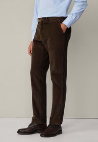 Pantalons en velours côtelé marron avec une coupe droite, dotés d'un devant plat et de poches latérales, assortis à des chaussures en cuir noir.