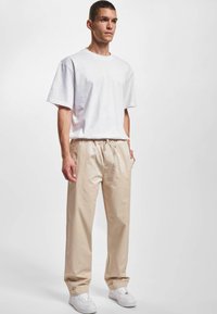 Tricou alb din bumbac cu mâneci scurte, asociat cu pantaloni bej de tip relaxed fit. Adidași albi completează ținuta cu o paletă de culori neutră.